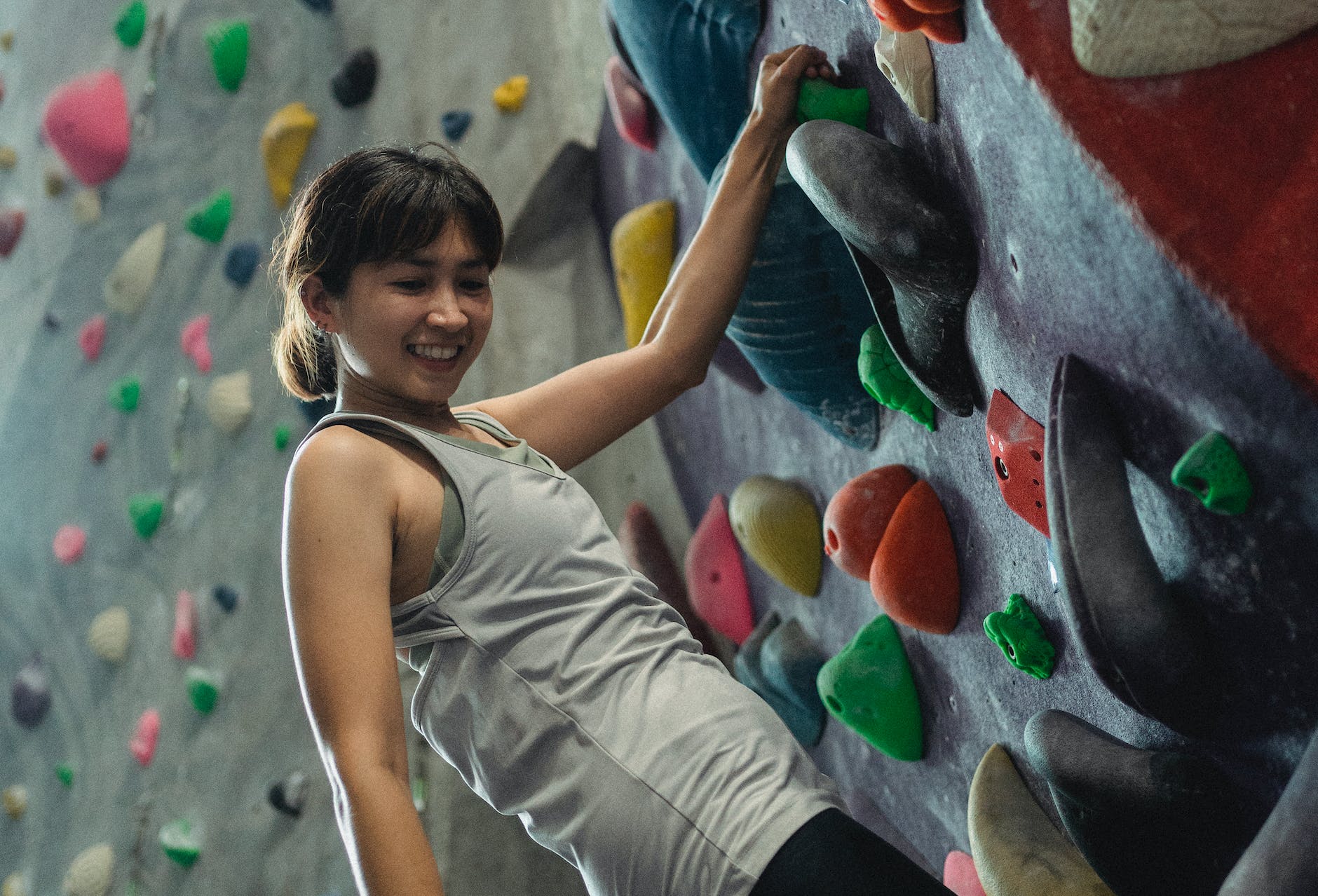 smiling asian woman climbing wall in modern gym